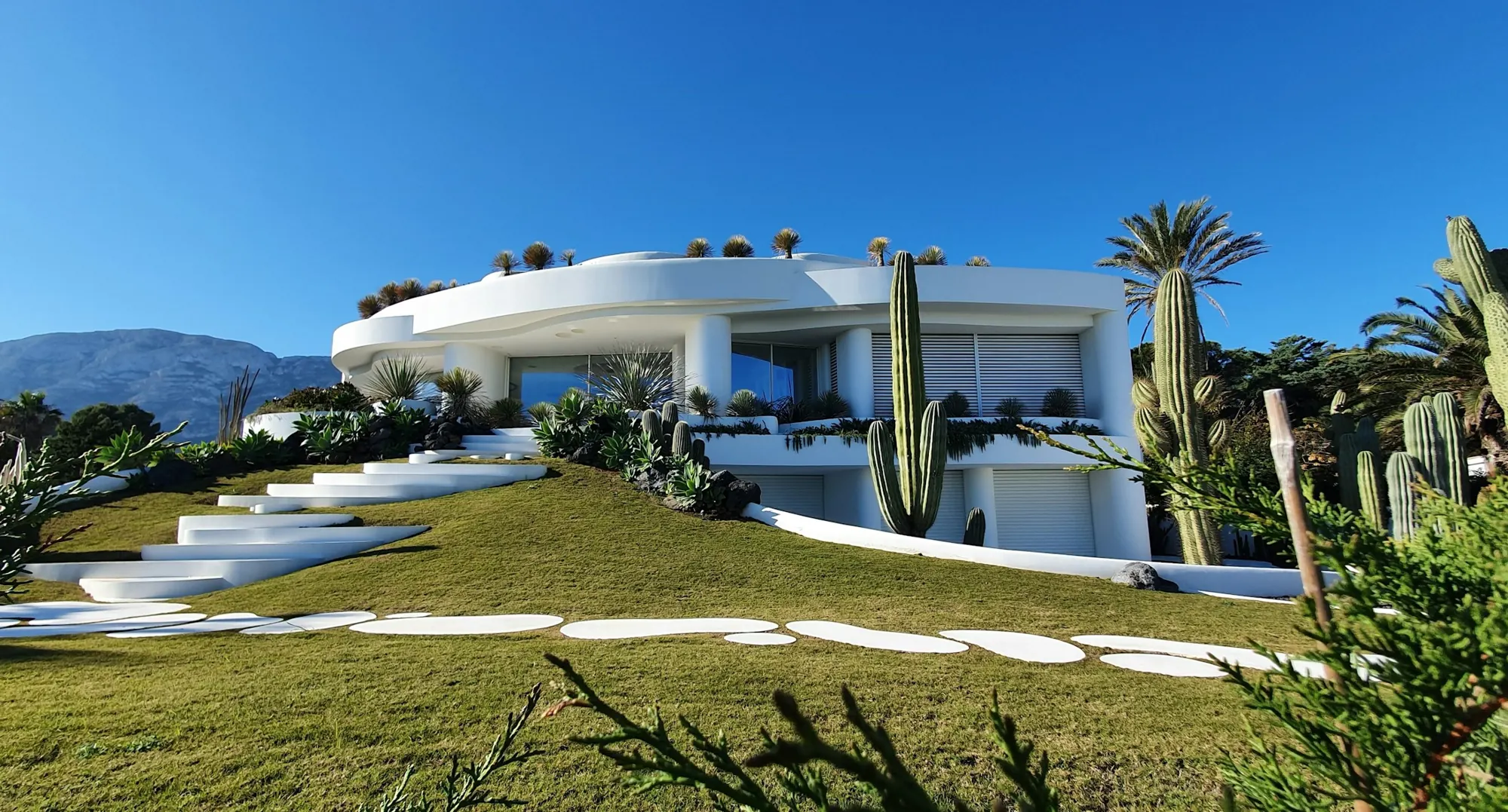 Casa blanca de formas curvas sobre una ladera de césped con cactus