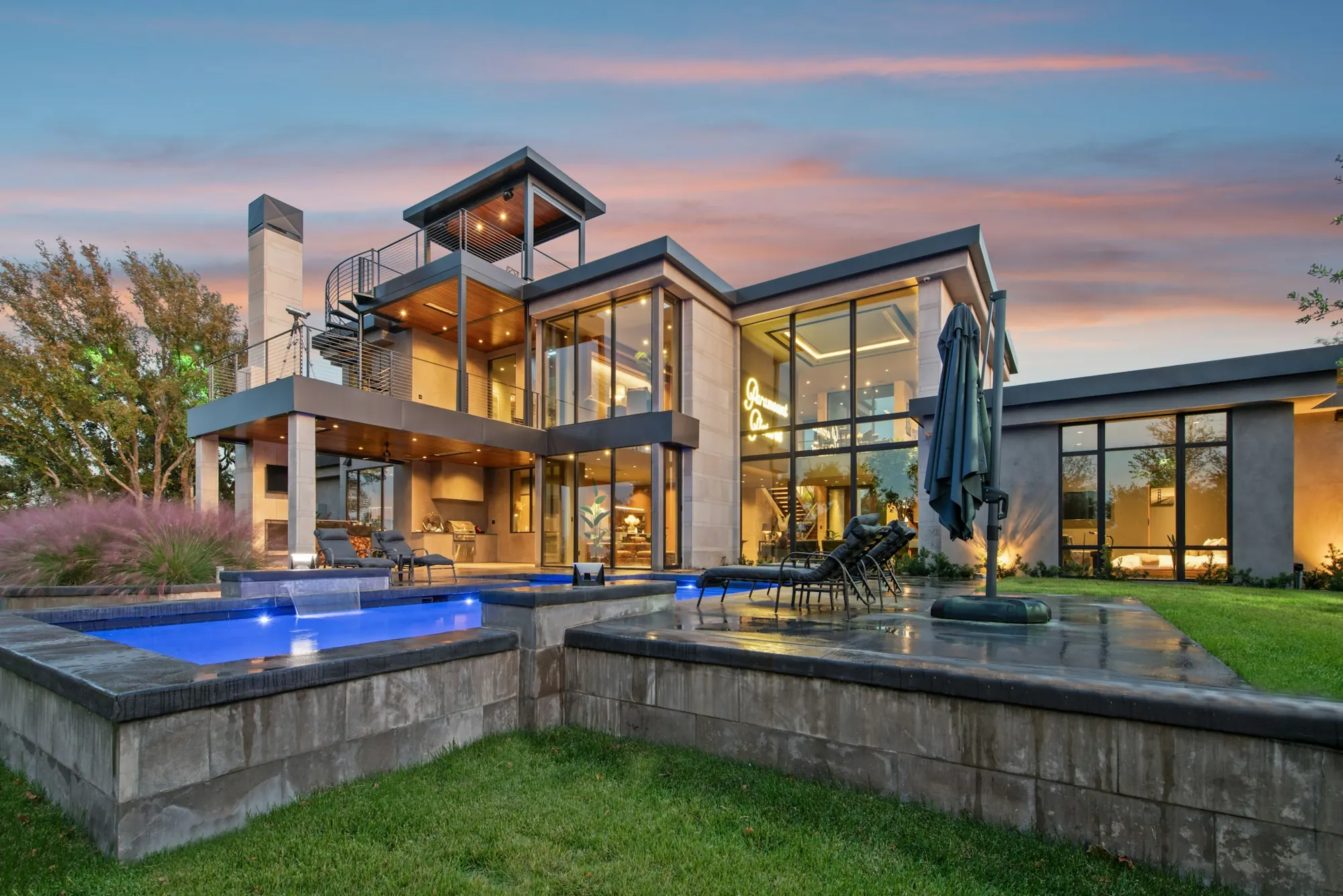 Casa de vidrio y piedra iluminada al atardecer con piscina
